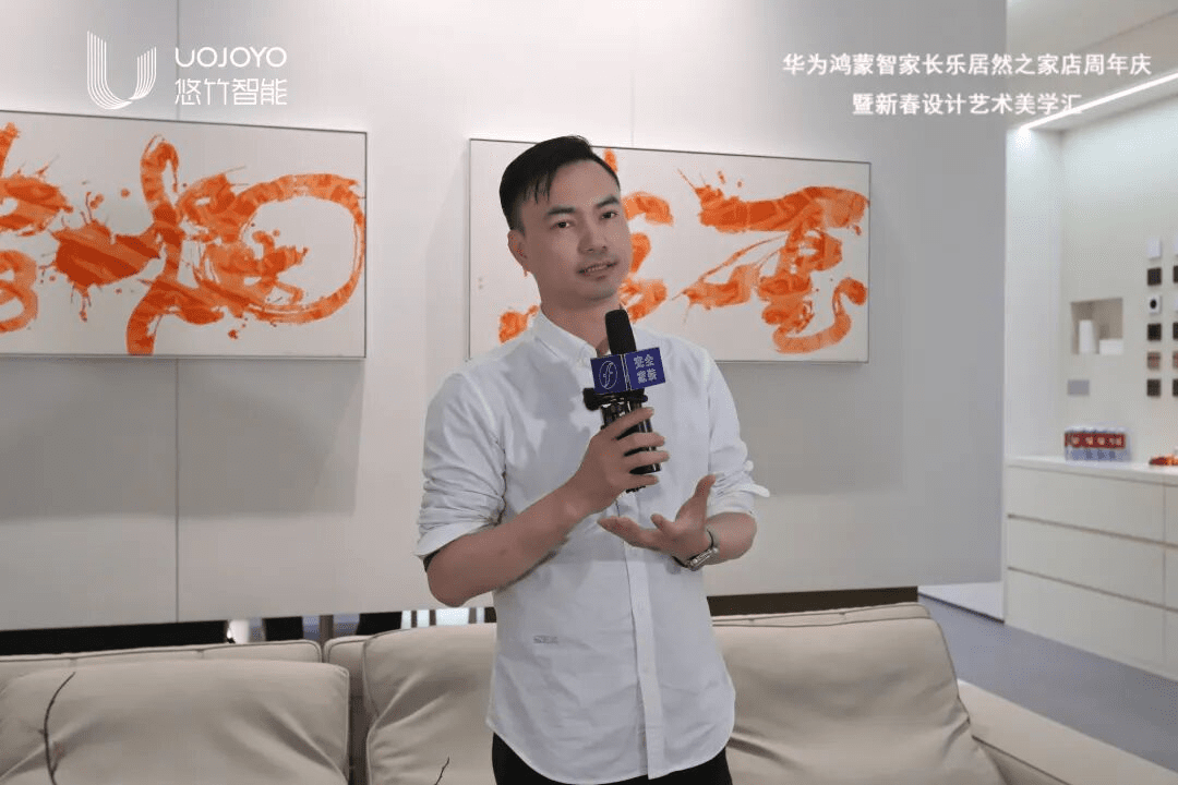 典尚装饰薛勇接受专访,穿着白色衬衫,手持带有紫金视频标识的麦克风,背景是橙色书法作品